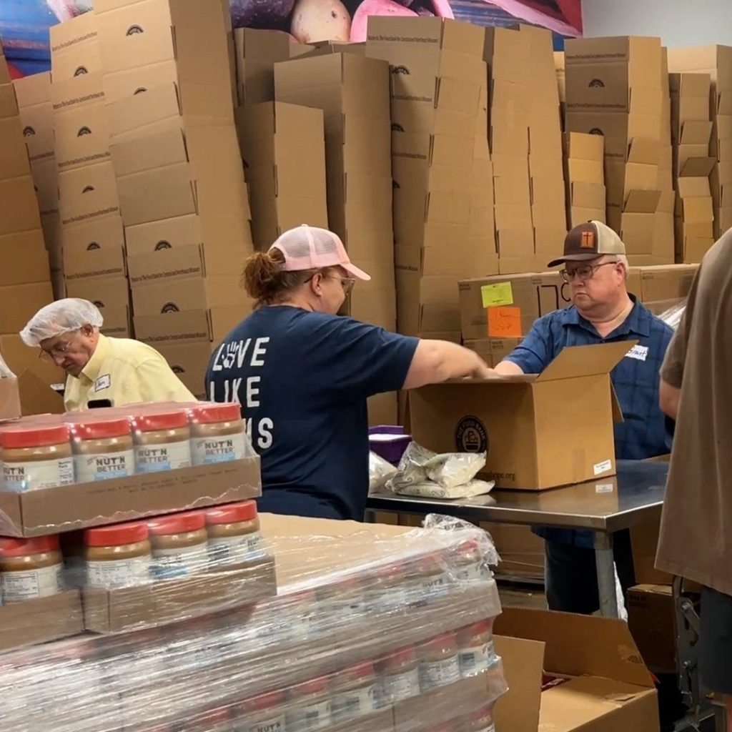 Three volunteers place items into a cardboard box.